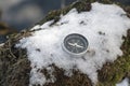 The compass is lying on the snow on the lake shore . The arrow points to the North