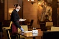 Competent waitress in protective mask preparing table Royalty Free Stock Photo