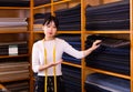 Competent young saleswoman offering various interesting cloth in textile shop