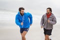 Competing with a Friend. two young men jogging together along the beach on an overcast morning.