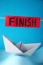 Competition concept. Paper boat among waves and red sign with word Finish on light blue background Royalty Free Stock Photo