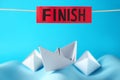 Competition concept. Paper boats among waves and red sign with word Finish on light blue background Royalty Free Stock Photo