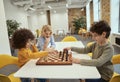 Competition. Joyful little diverse boys sitting at the table and playing chess in school Royalty Free Stock Photo