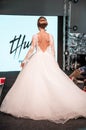 Competition of wedding stylists. A model in a white wedding dress with an open back and with a hairdo walks along the