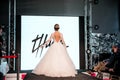 Competition of wedding stylists. A model in a white wedding dress with an open back and with a hairdo walks along the