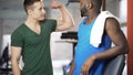 Competitive athletic men comparing and boasting biceps muscles, friends in gym