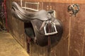 Competitive saddle of dark brown leather hanging on the bracket