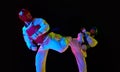 Competitive strong young men, taekwondo, karate athletes in motion, fighting, training against black background in neon