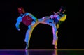 Competitive strong young men, taekwondo, karate athletes in motion, fighting, training against black background in neon