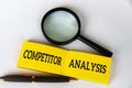 Competitor analysis text on yellow notepad with pen and magnifying glass on white background. Competitor analysis Royalty Free Stock Photo