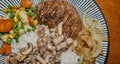 Complete meal of a grilled pork steak with roasted onions, vegetable mix of peas, carrots, corn and cauliflower, on rice with