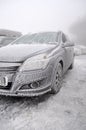 Completely frozen and snow-covered passenger car in a parking lot in winter in a thick fog