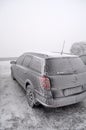 Completely frozen and snow-covered passenger car in a parking lot in winter in a thick fog