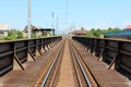 Completely rusted metal railway bridge leading to railway station filled with electrical poles and abandoned buildings