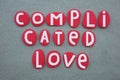 Complicated love, creative text composed with red painted stone letters over green sand