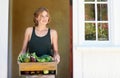 Compliments of the season. A young woman holding a crate of vegetables outdoors.