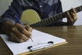 Composer holding pencil and writing lyrics in paper. Musician playing acoustic guitar