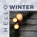 Composite of hello winter text and high angle view of candles, pinecone and leaves on table