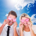 Composite image of attractive young couple holding pink hearts over eyes Royalty Free Stock Photo