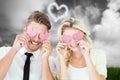 Composite image of attractive young couple holding pink hearts over eyes Royalty Free Stock Photo