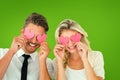 Composite image of attractive young couple holding pink hearts over eyes Royalty Free Stock Photo