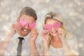 Composite image of attractive young couple holding pink hearts over eyes Royalty Free Stock Photo