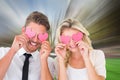 Composite image of attractive young couple holding pink hearts over eyes Royalty Free Stock Photo