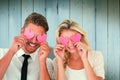 Composite image of attractive young couple holding pink hearts over eyes Royalty Free Stock Photo