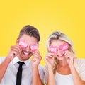 Composite image of attractive young couple holding pink hearts over eyes Royalty Free Stock Photo