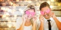 Composite image of attractive young couple holding pink hearts over eyes Royalty Free Stock Photo