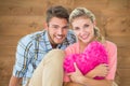 Composite image of attractive young couple sitting holding heart cushion Royalty Free Stock Photo