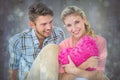 Composite image of attractive young couple sitting holding heart cushion Royalty Free Stock Photo