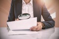 Composite image of businesswoman looking at document through magnifying glass Royalty Free Stock Photo