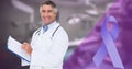 Composite image of cancer ribbon and caucasian smiling mature male doctor standing with clipboard Royalty Free Stock Photo