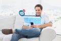 Composite image of cheerful man sitting on the couch using his smartphone Royalty Free Stock Photo