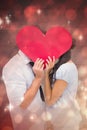 Composite image of couple covering their kiss with a heart