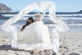 Composite image of couple sitting on the beach under blanket looking out to sea Royalty Free Stock Photo