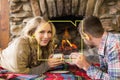 Composite image of couple with tea cups in front of lit fireplace