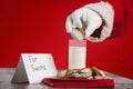 Composite image of cropped image of santa claus dipping cookies in glass of milk