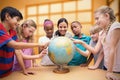 Composite image of cute pupils and teacher looking at globe in library Royalty Free Stock Photo