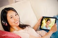 Composite image of girl using her tablet pc on the sofa and listening to music smiling at camera Royalty Free Stock Photo