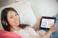 Composite image of girl using her tablet pc on the sofa and listening to music smiling at camera Royalty Free Stock Photo