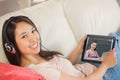 Composite image of girl using her tablet pc on the sofa and listening to music smiling at camera Royalty Free Stock Photo