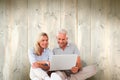 Composite image of happy couple sitting and using laptop Royalty Free Stock Photo