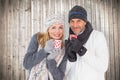 Composite image of happy couple in winter fashion holding mugs