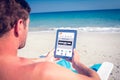 Composite image of man using digital tablet on deck chair at the beach Royalty Free Stock Photo