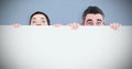 Composite image of man and woman hiding behind a white board with room for copy space Royalty Free Stock Photo