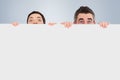 Composite image of man and woman hiding behind a white board with room for copy space Royalty Free Stock Photo