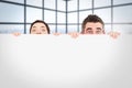 Composite image of man and woman hiding behind a white board with room for copy space Royalty Free Stock Photo