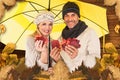 Composite image of portrait of couple holding autumn leaves while standing under yellow umbrella Royalty Free Stock Photo